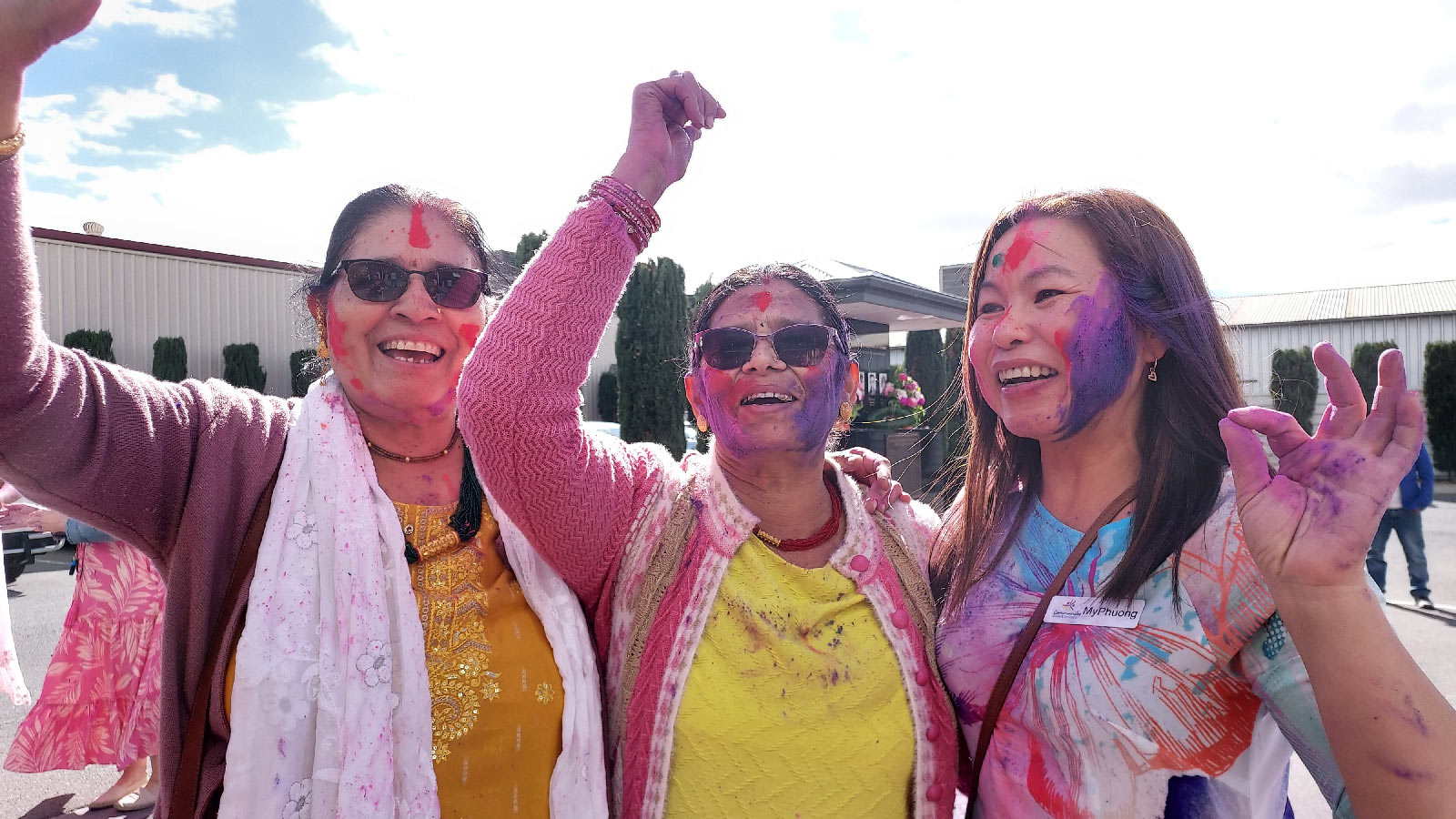 Three women with arms raised, faces painted with coloured powder, happy, laughing.